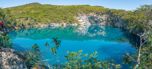 View of the Cenote of Candelaria in Huehuetenango, Guatemala, on a sunny day where you can see the turquoise color of the water and the reflection of the trees in the water.