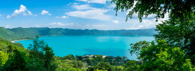 Panoramic view of the beautiful lake of Coatepeque in El Salvador, with a blue sky, in the season where its waters are turquoise and most of its mountains and vegetation are green. - obrazy, fototapety, plakaty
