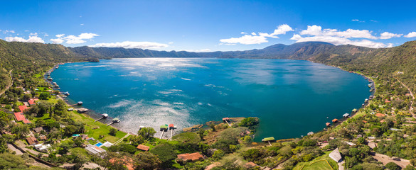 Panoramic view of the beautiful lake of Coatepeque in El Salvador, with a blue sky, in the season where its waters are turquoise and most of its mountains and vegetation are green.