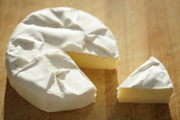 Whole camembert cheese and one slice on a wooden table