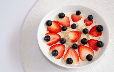 oatmeal with beautifully laid strawberries and blueberries in a white plate on a white tablecloth