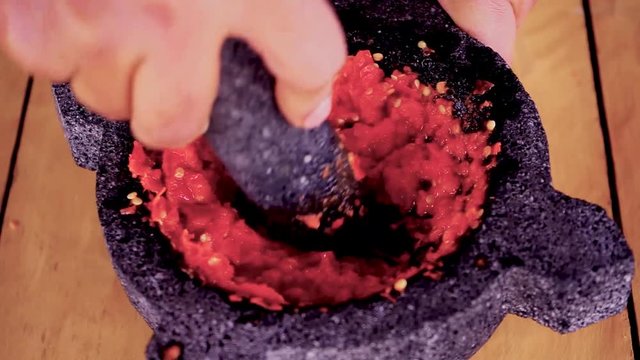 Using a morter to mash red hot chilli peppers