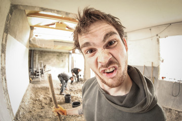 A worker making a stupid face while renovating a house. Other workers in a background. fisheye view.