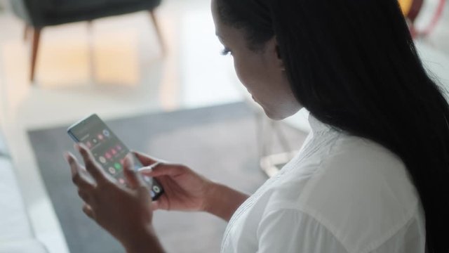 African American woman hands searching for apps on her smart phone, browsing for software application. Technology problems for black people using finger with cell phone. Over the shoulder view