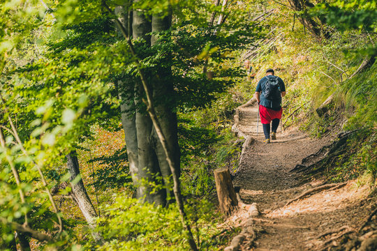 A seriously overweight person is descending down the mountain using hiking poles. Concept photo of a man loosing weight while hiking in the mountains. Sport, fitness and health.