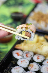 Hand chopstick sushi california uramaki avocado salmon soy sauce bowl take away, delivery, green towel tropical summer japanese food vertical