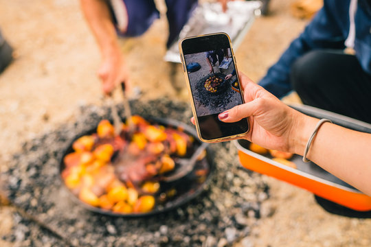 A woman taking a photo of Sach, sac or sache, a traditional balkan meal prepared in pots covered with charcoal. Photographing a podpeka meal with a telephone