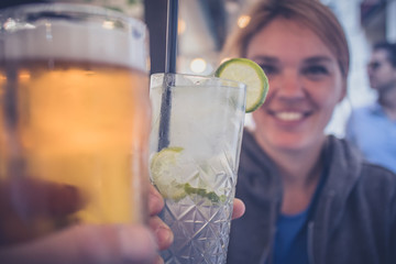 A young caucasian woman enjoying a glass of gin tonic with a lime and cheering with another person...
