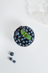 Fresh juicy blueberries with a sprig of mint in a white bowl with lace fabric on a white background. Flat lay