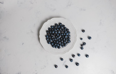 Fototapeta na wymiar Fresh juicy blueberries in a white plate on a gray background. Flat lay