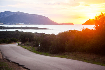 Early morning view of Golfo Aranci on Sardinia, looking towards the ferry port with a ferry visible. Asphalt road in the foreground, sun is about to rise.
