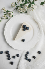Obraz na płótnie Canvas Blueberry cheesecake on a white plate, lace fabric and a branch with white flowers. 