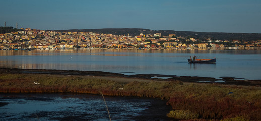 Panorama of the city of Sant Antioco with a lagoon and a fishing boat visible on th esea. Romantic sunny morning picture of a village on Sardinia.