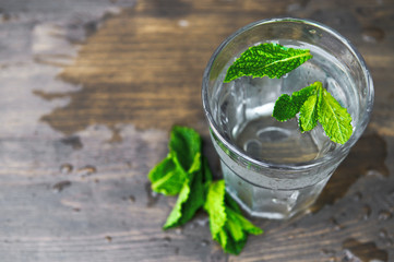 Pure cold water with mint petals on a wooden background. Detox theme. Selective focus.