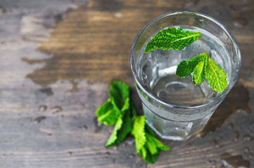 Pure cold water with mint petals on a wooden background. Detox theme. Selective focus.