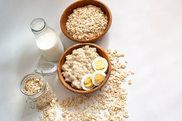 cooked oat flakes in a wooden bowl with milk  white background