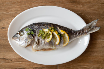 Dorada fish fried with lemon and parsley on a white plate