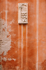 Close-ups of building facades in Venice, Italy. Stone bas-relief on a small stone rectangular plank, on an orange wall on the facade of the building.