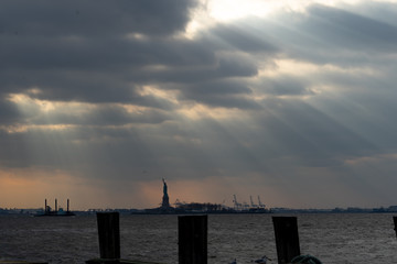 view of the statue of liberty from Manhattan New York on a cloudy afternoon with beautiful sun rays