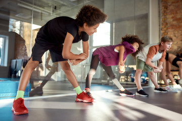 Join us to see results. Portrait of a boy smiling while warming up, exercising together with other kids in gym. Sport, healthy lifestyle, active childhood concept