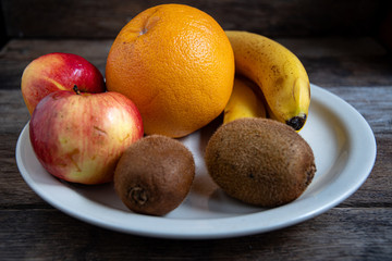 Kiwi, banana, apple, grapefruit in a white plate on the kitchen table. Cooking fruit salad in the home kitchen.
