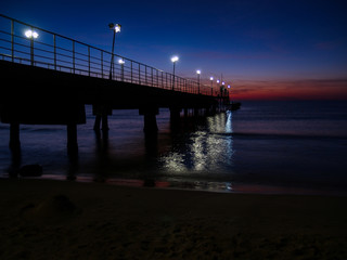 Obraz premium night sea landscape. the pier is lit by lanterns. Silhouettes of beach umbrellas and sunbeds.