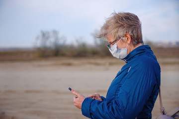 Pensioner in a face medical mask holding a smartphone  during the coronavirus epidemic. Infection protection concept