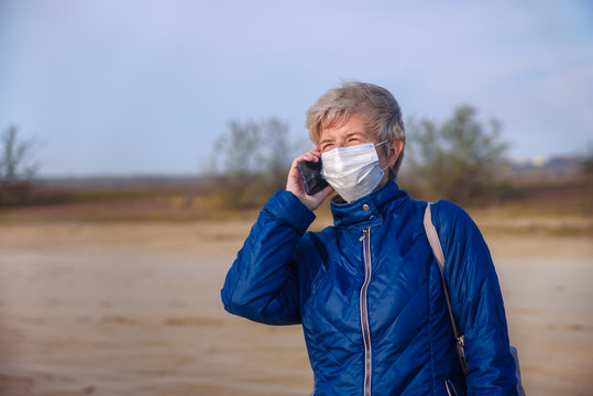 Happy smiling senior woman talking on a cell phone in a face mask during the coronavirus epidemic. Infection protection