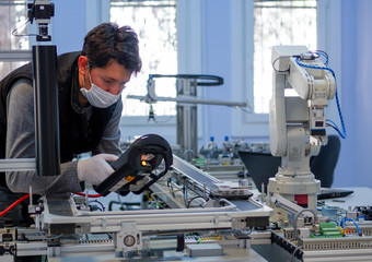 Man with surgical mask on face against COVID-19 ( Coronavirusis ) programming robot arm with control panel which is integrated on smart factory production line. industry 4.0 automation line.