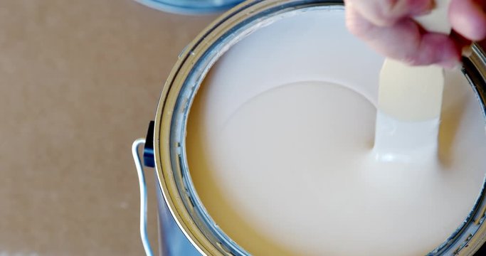 Hand stirring white paint with wooden stick in container, preparing fresh can of paint close-up, 4k