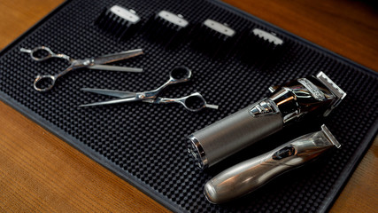 Scissors, electric hair trimmers and four different nozzles lying on a rubber mat in the barbershop. Professional barber tool kit