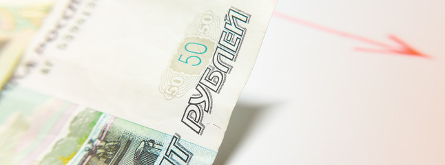 Russian currency and regressive chart. A bill of fifty Russian rubles and a red graph with an arrow. The concept of the Fall in the price of the Russian ruble, falling oil prices.