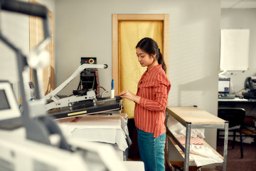 Printing expert. Young cheerful female worker using heat press transfer machine for printing...