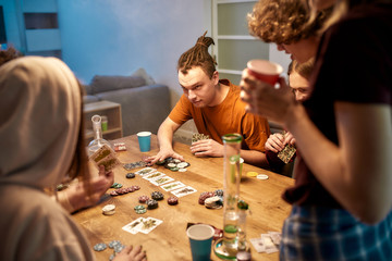 Going all in. Young people playing poker after smoking marijuana at home. Marijuana tools, bong on the table. Home party