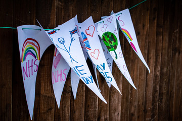 Chinnor, United Kingdom - 8 May 2020: Homemade drawn happy bunting flags for VE day in United Kingdom, patriotic children drawings hanging on a wodden fence, kids tribute to National Health Service