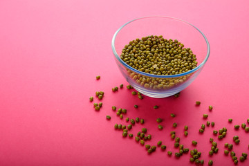 Glass jar with green cereal mung bean on a pink background.