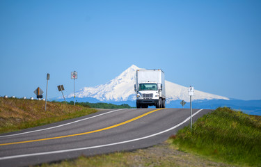 Big rig day cab semi truck with box trailer running on the road with snow mountain on the background