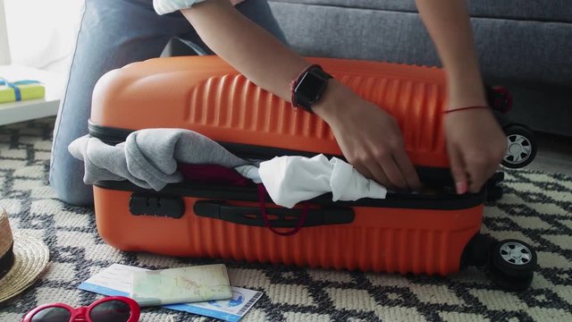 Cute girl standing on her knees on overfilled orange suitcase, trying to close it