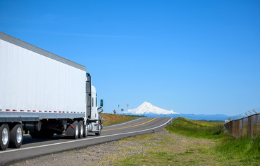 Big rig white semi truck transporting cargo in dry van semi trailer running on the narrow road with...