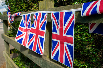 Fototapeta na wymiar Union Jack bunting on a fence, three flags in row on a string, english ivy by the flags, VE day decorations in UK, memorial symbol of winning second world war, celebration time
