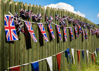 Union Jack bunting on a fence row, many flags in row on a string, triangular flags, front of garden VE day decorations in UK, memorial symbol of winning second world war