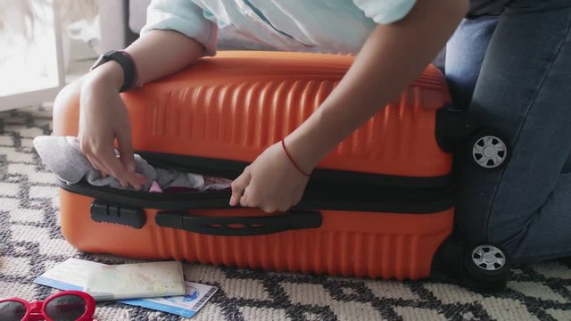 Young girl standing on elbowson on overfilled orange suitcase, trying to close it