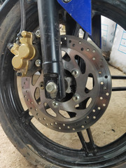 Closeup detail of a racing motorcycle's front wheel. This is the brake cliper, rotor, rim, tire, and suspension. Selective Focus