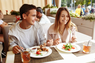 A cheerful and beautiful couple are relaxing on a summer terrace in a restaurant with food and drinks. The guy and the girl have fun on the terrace