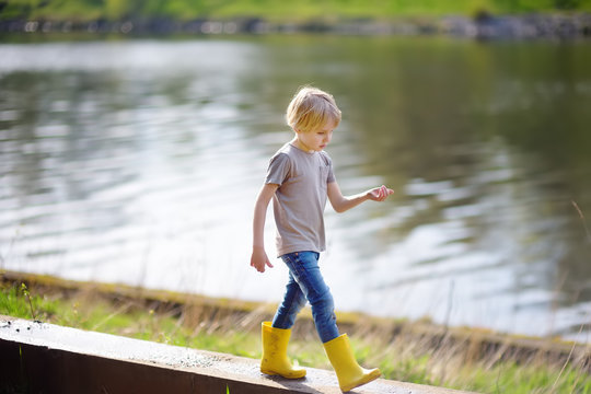 Preschooler Child Wearing Yellow Rain Boots Walking Near River After Rain. Kid Playing And Having Fun In Sunny Spring Or Summer Day.