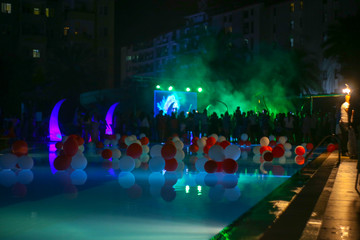 Fototapeta na wymiar Decorated pool by the hotel. Blurred silhouette of people from the concert. bright lights. Rest in hot countries.