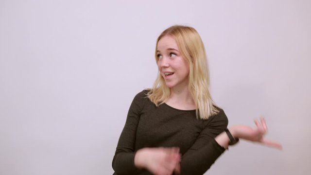 Young Blonde Woman In Black Sweater With Stylish Watch On White Background, Happy Attractive Girl Smiling Points forefinger At The Person nearby. Concept Of Guilty People And Charges