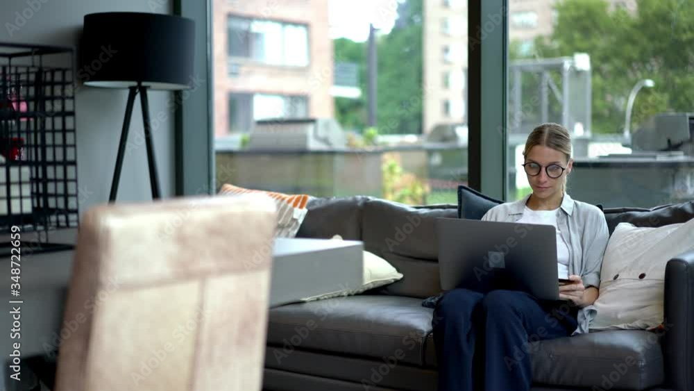 Poster young woman resting on comfortable couch and making payment for booking tickets on website in modern