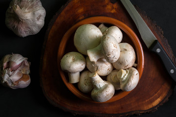 Top view of a bowl with mushrooms next to some garlic on a dark background