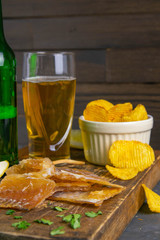 Dried cod fillet with beer, lemon and potato chips on dark wooden board. Snack on fish with beer....